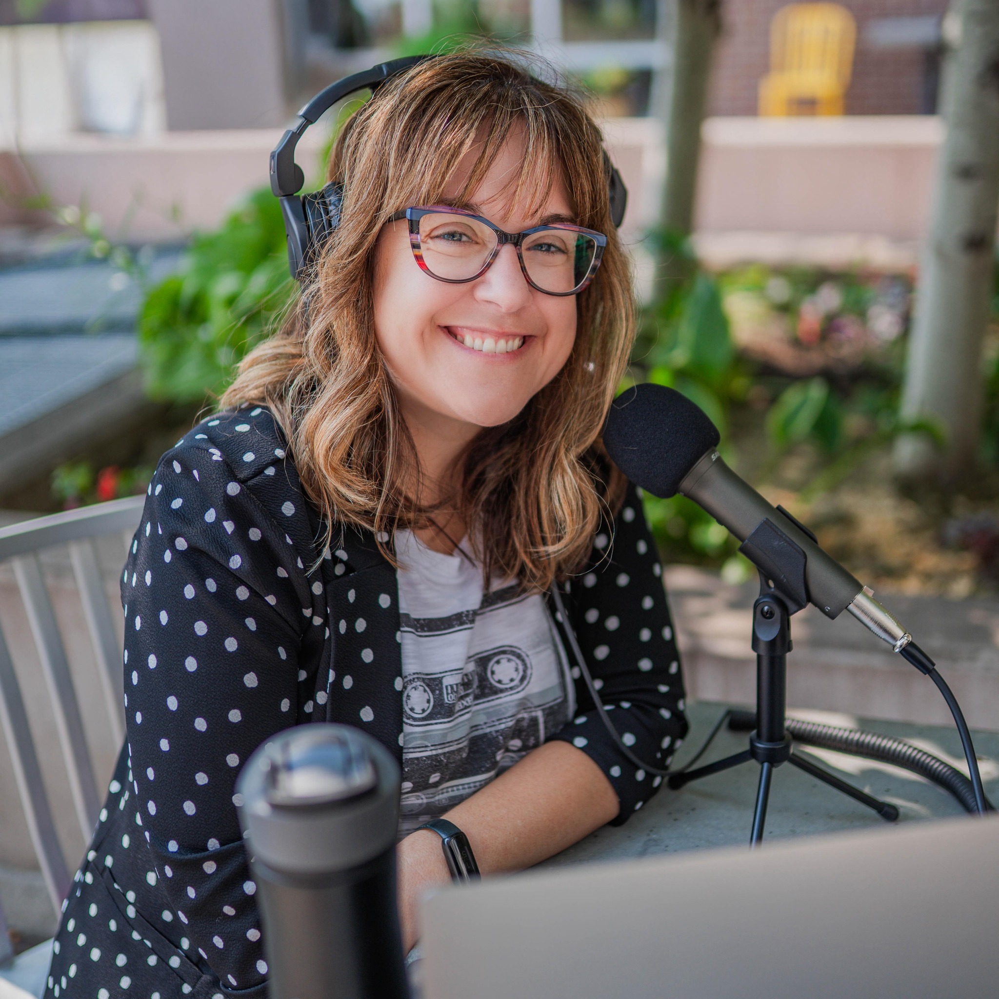 Natasha sitting in front of microphone and laptop. Wearing a polka dot blazer.